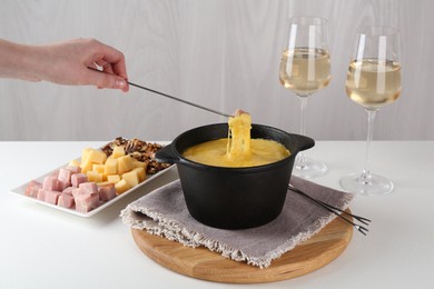 Photo of Dipping piece of ham into fondue pot with tasty melted cheese at white table, closeup