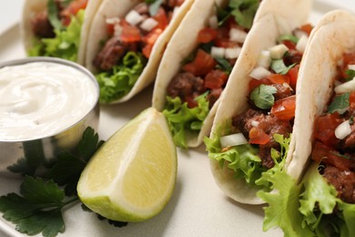 Photo of Delicious meat tacos with vegetables, lime and sauce on light table, closeup