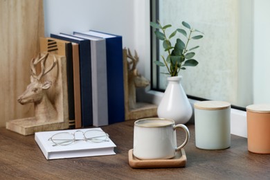 Photo of Cup of coffee with books and home decor on wooden window sill