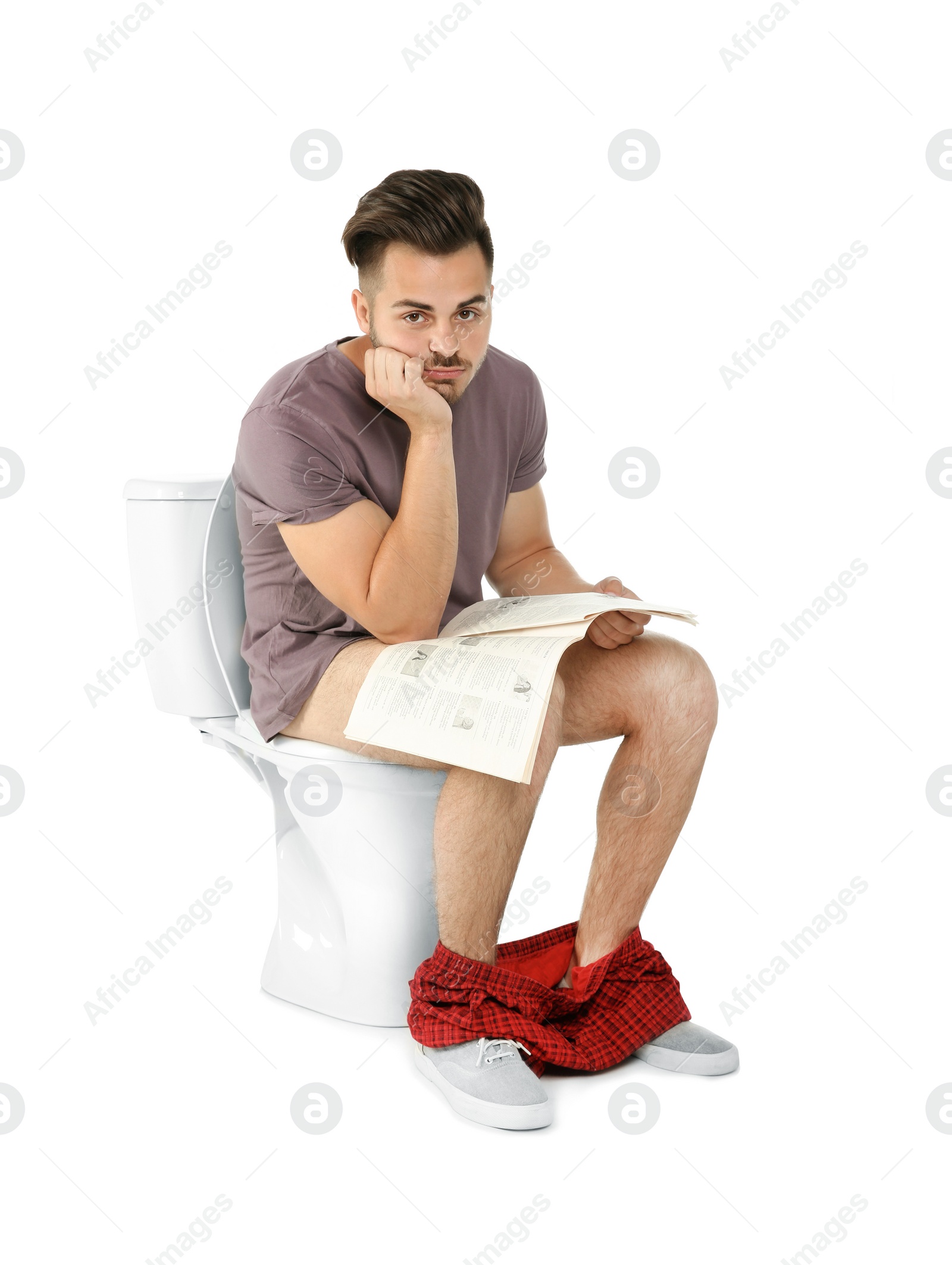 Photo of Young man with newspaper sitting on toilet bowl. Isolated on white