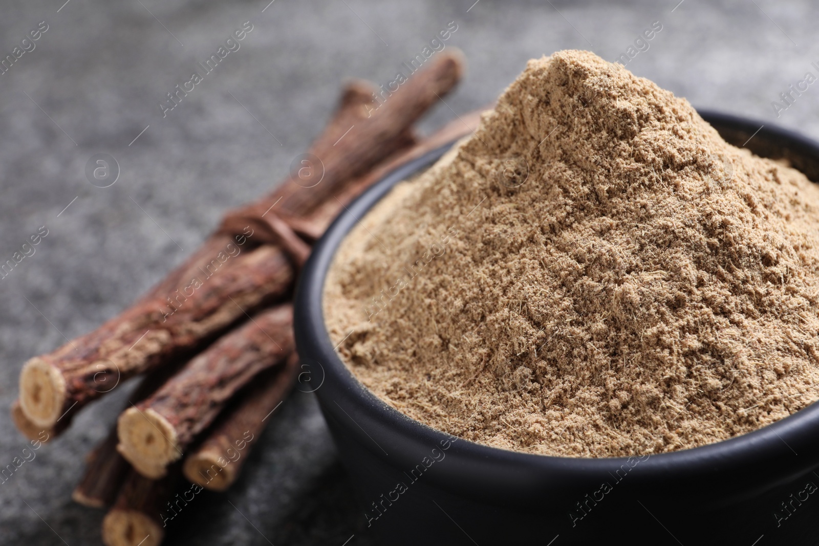 Photo of Liquorice powder and dried sticks on grey table, closeup. Space for text