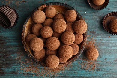 Plate with chocolate truffles on wooden background, top view