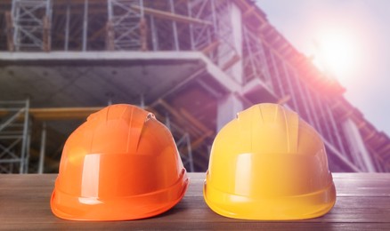 Image of Hard hats on wooden surface at construction site with unfinished building 