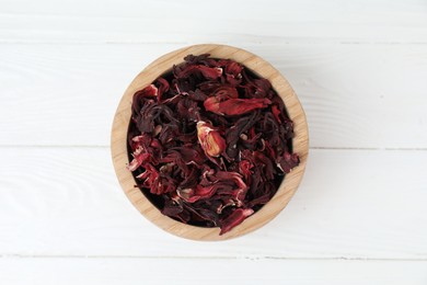 Photo of Hibiscus tea. Bowl with dried roselle calyces on white wooden table, top view