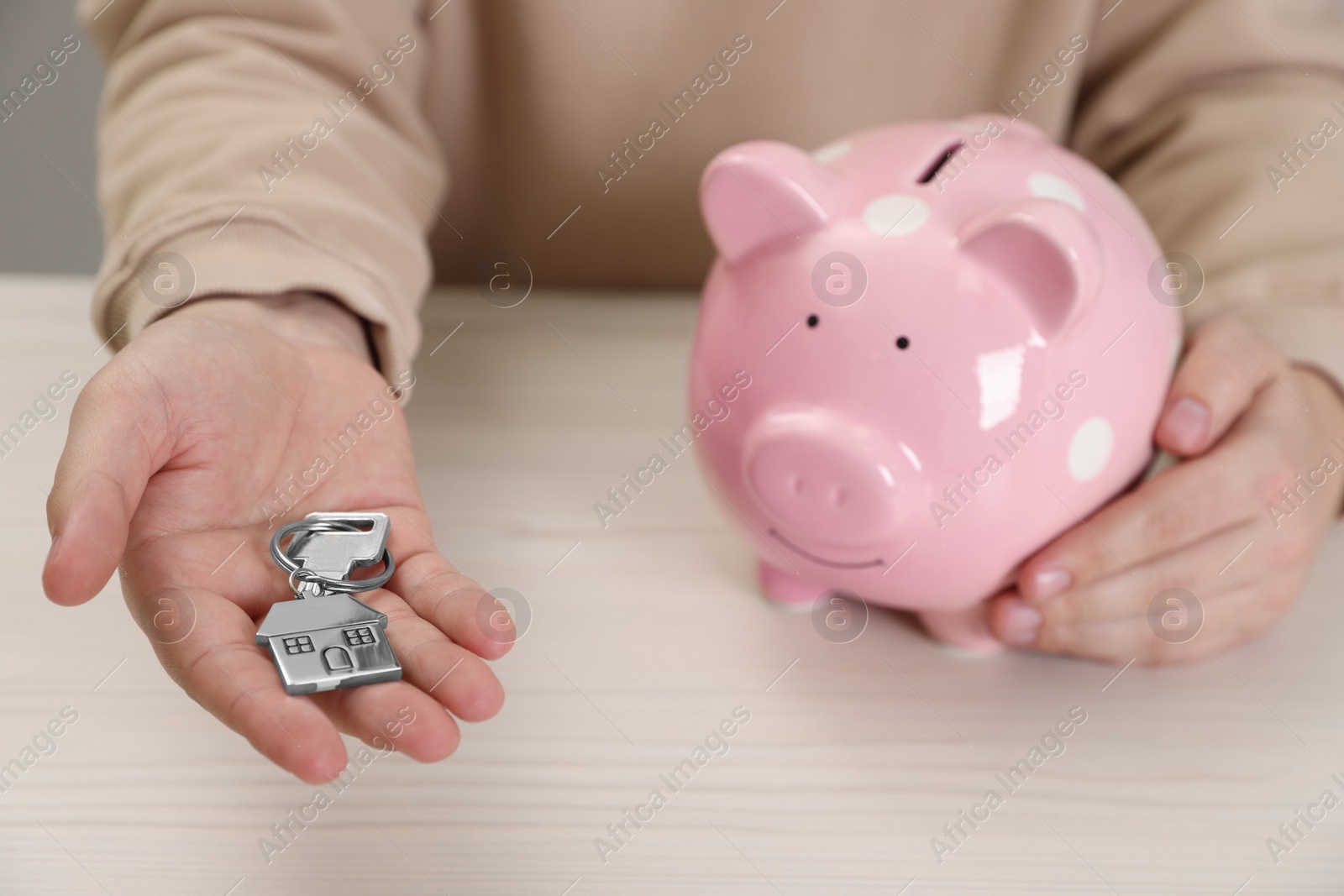 Photo of Man holding key and piggy bank at wooden table, closeup. Saving money for buying house