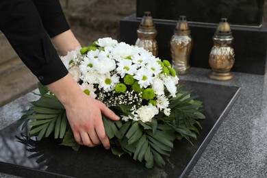Photo of Woman putting funeral wreath of flowers on granite tombstone outdoors, closeup