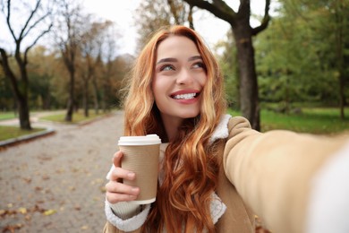 Photo of Portrait of happy woman with paper cup taking selfie in autumn park