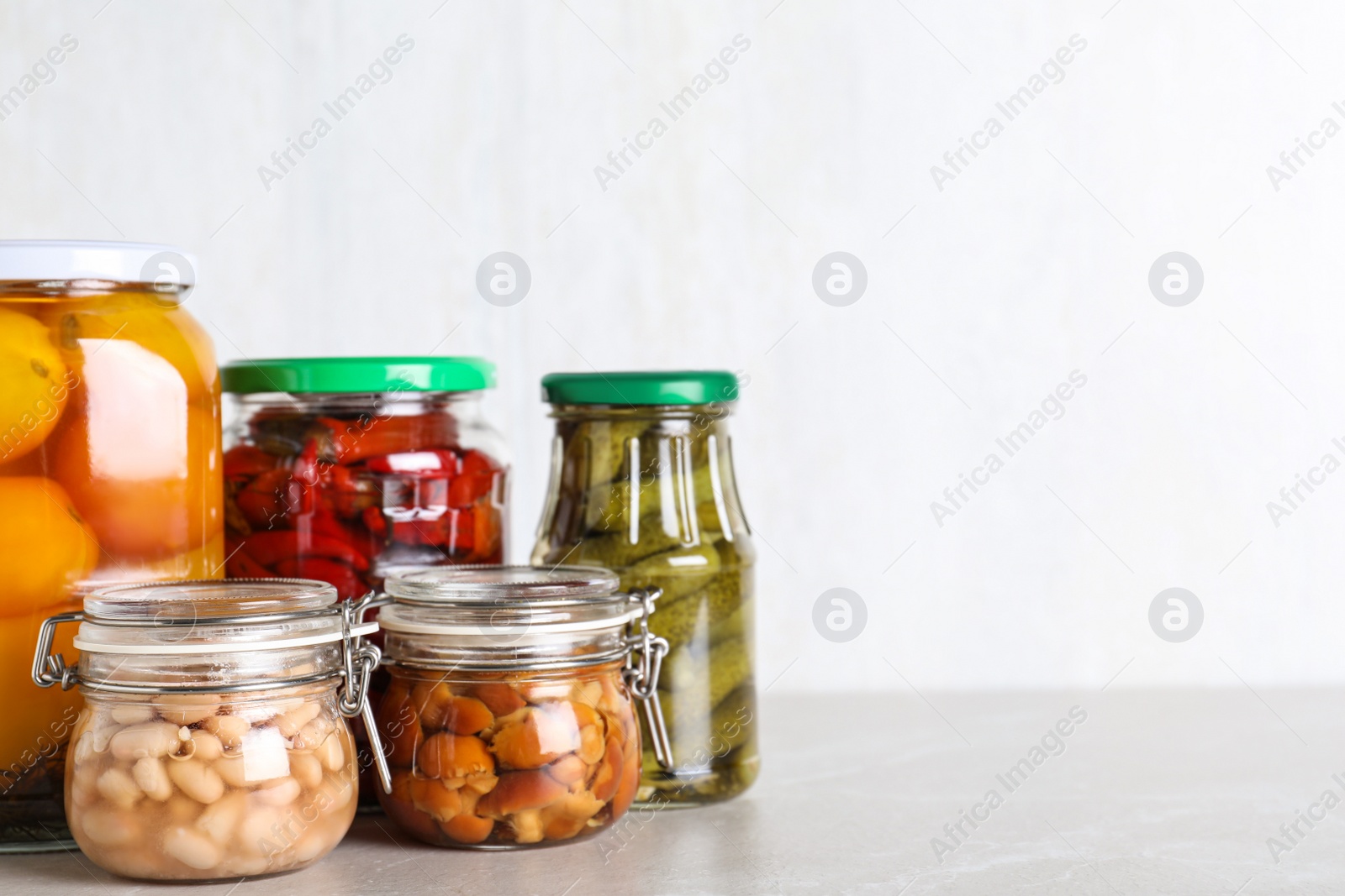 Photo of Glass jars with different pickled vegetables on light marble table. Space for text