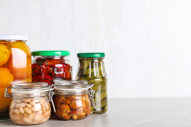 Photo of Glass jars with different pickled vegetables on light marble table. Space for text