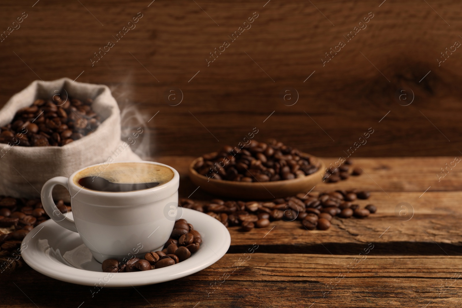 Image of Cup of aromatic hot coffee and beans on wooden table, space for text