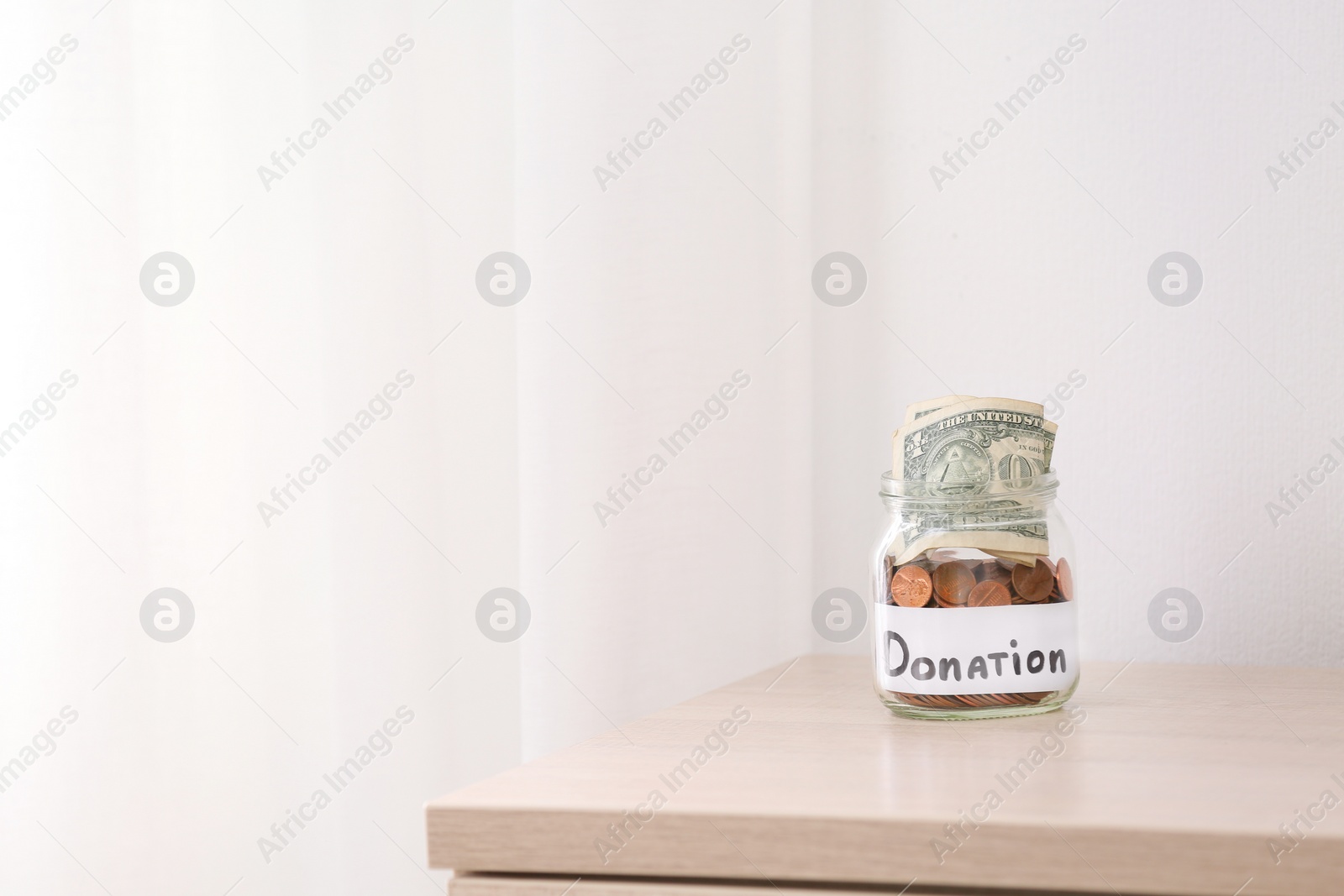 Photo of Glass jar with money and label DONATION on table against light background. Space for text
