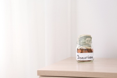 Photo of Glass jar with money and label DONATION on table against light background. Space for text