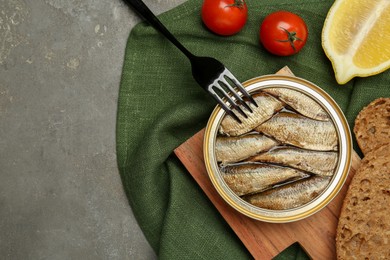 Canned sprats, tomatoes, lemon, bread and fork on grey table, flat lay. Space for text