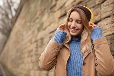 Photo of Young woman with headphones listening to music near stone wall. Space for text