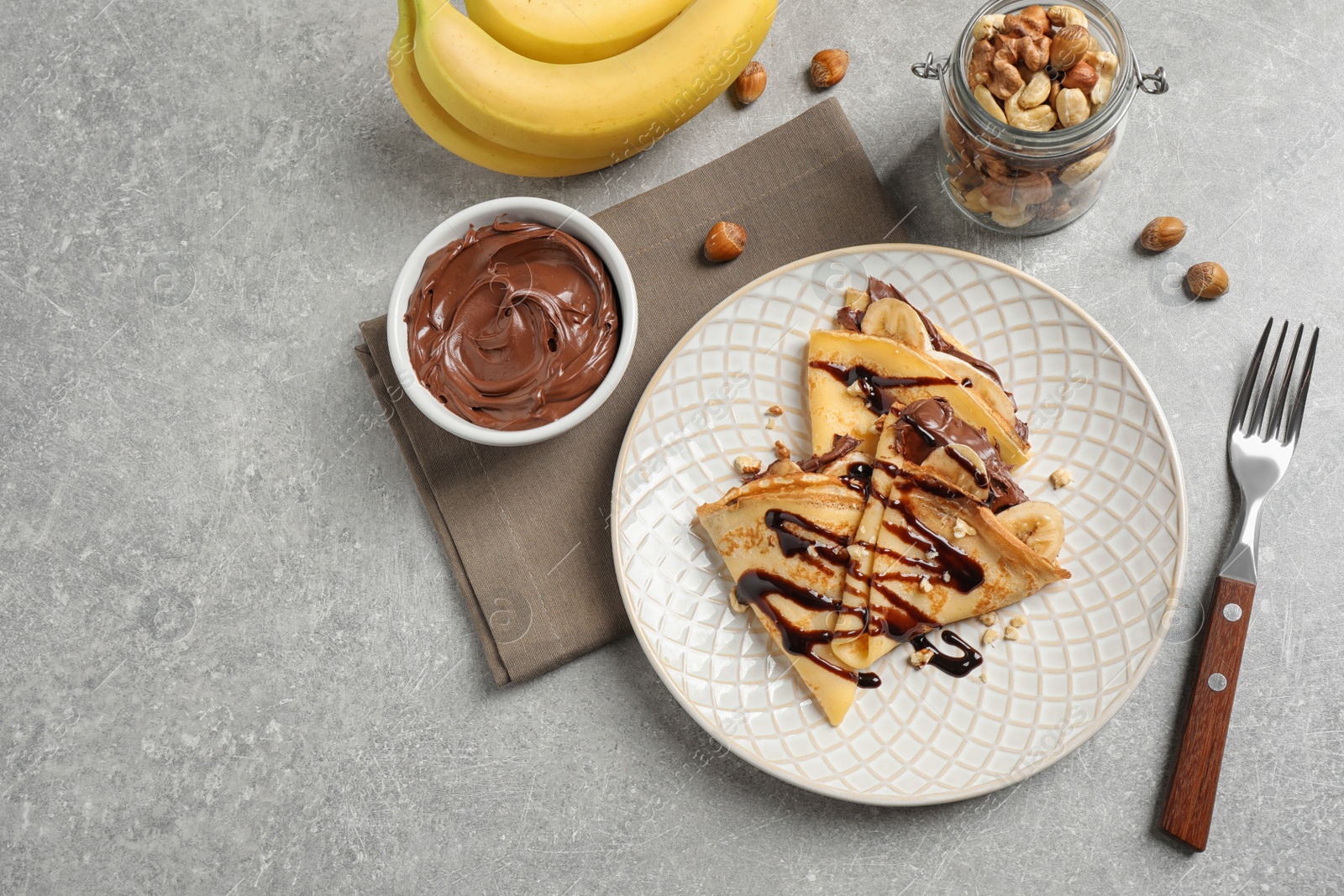 Photo of Delicious thin pancakes with chocolate spread, banana and nuts on light table, flat lay
