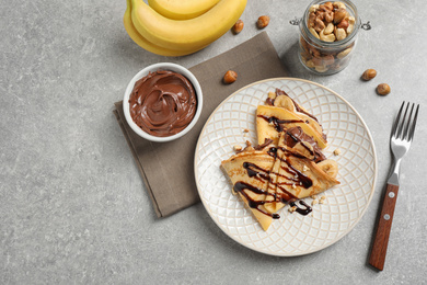 Delicious thin pancakes with chocolate spread, banana and nuts on light table, flat lay