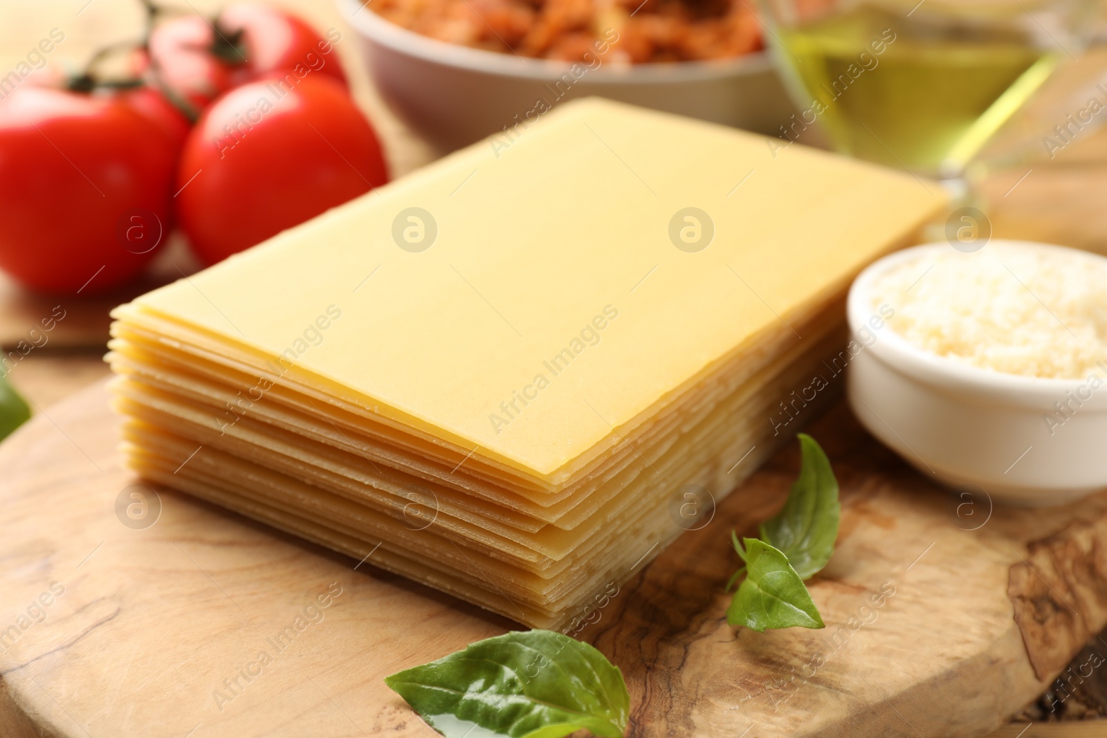 Photo of Cooking lasagna. Wooden board with pasta sheets and basil leaves on table, closeup