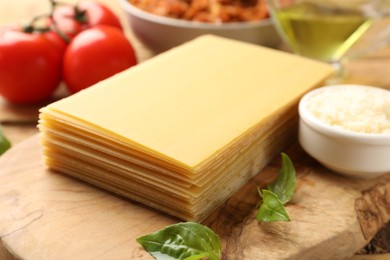 Cooking lasagna. Wooden board with pasta sheets and basil leaves on table, closeup