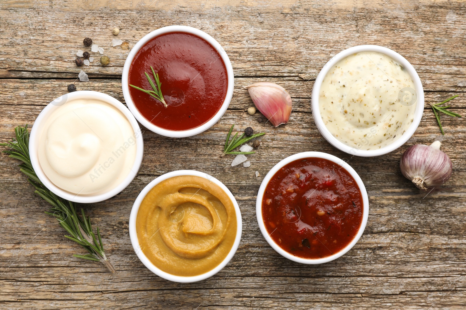 Photo of Different tasty sauces in bowls, herbs and spices on wooden table, flat lay