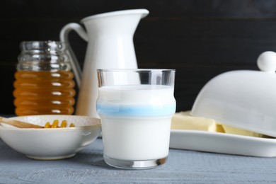 Photo of Glass with milk, honey and butter on grey wooden table