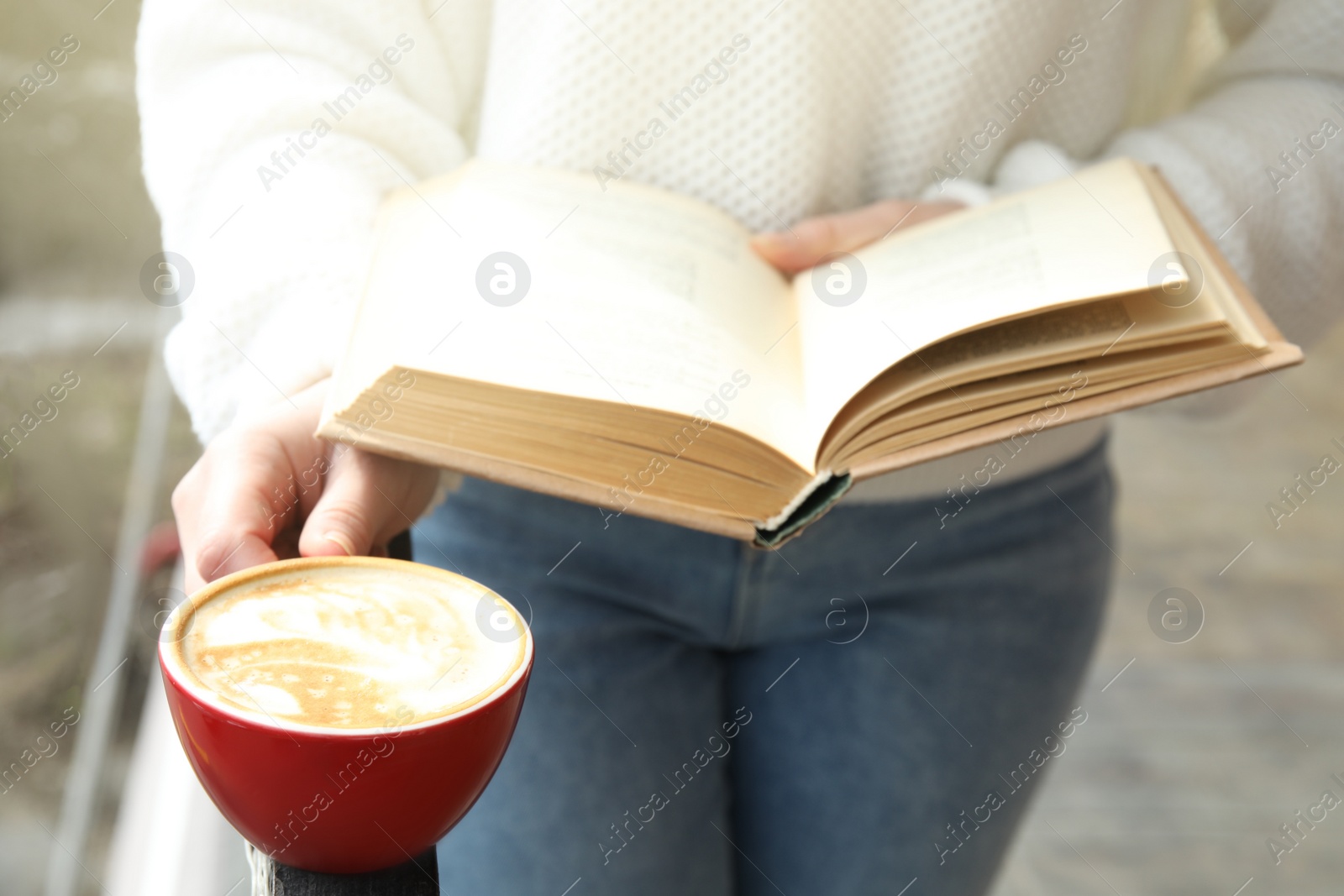 Photo of Woman with cup of coffee reading book outdoors, closeup