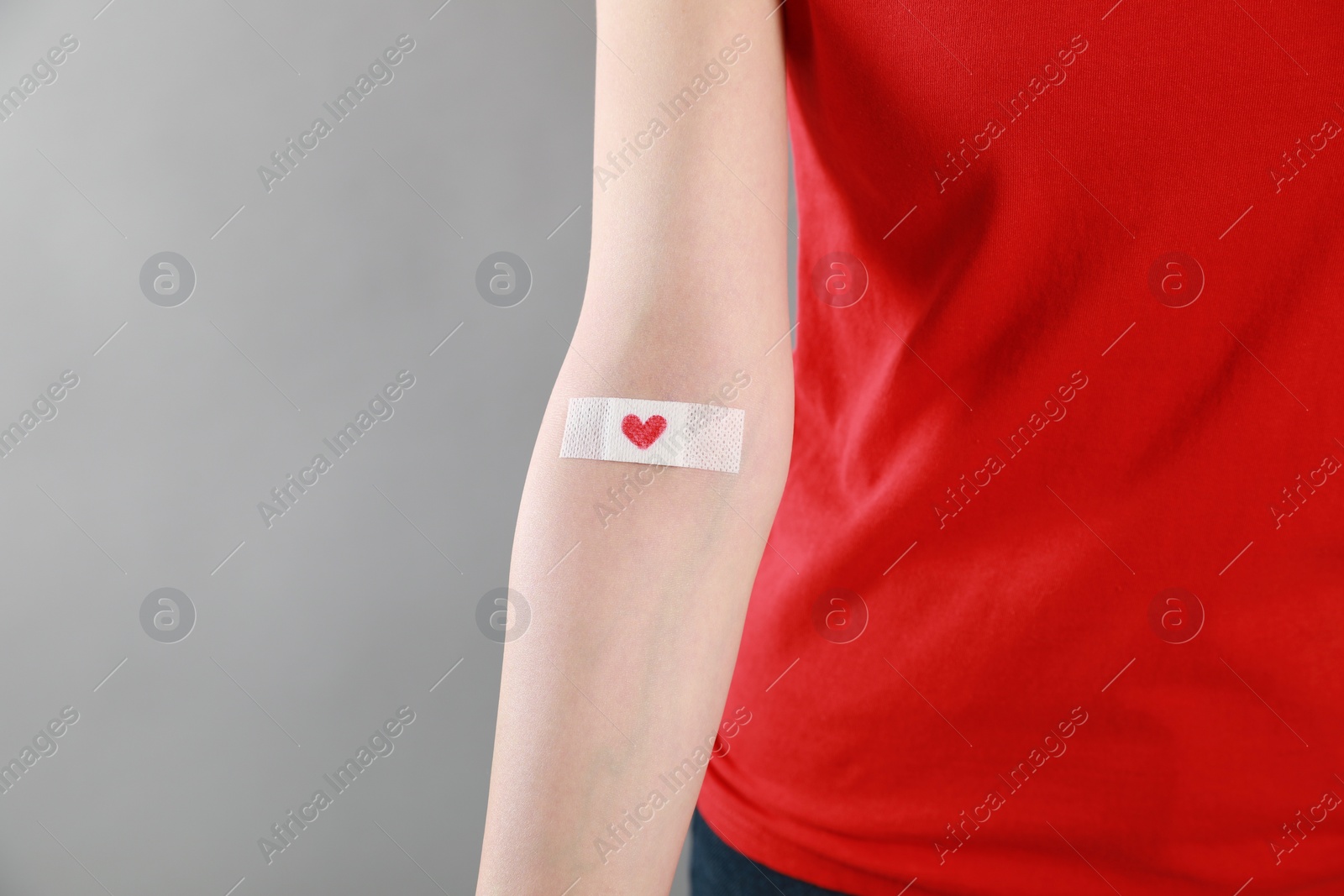 Photo of Blood donation concept. Woman with adhesive plaster on arm against grey background, closeup. Space for text