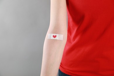 Photo of Blood donation concept. Woman with adhesive plaster on arm against grey background, closeup. Space for text