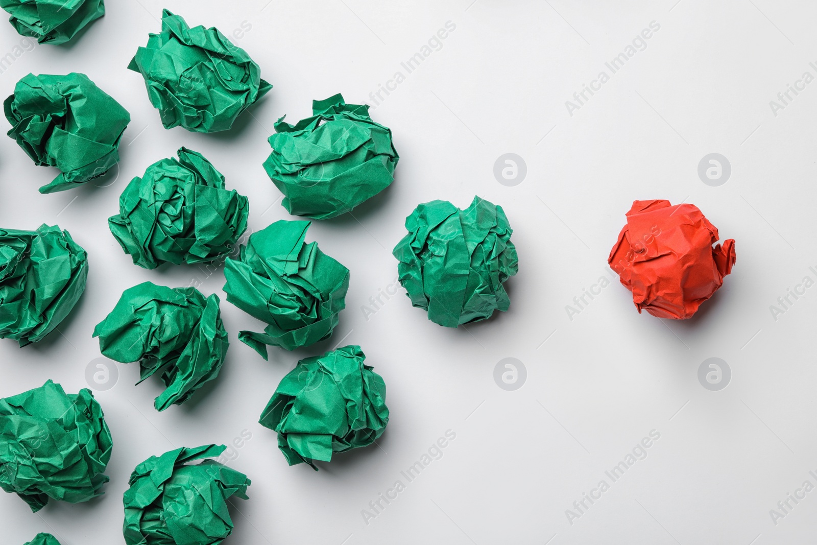 Photo of Green balls of crumpled paper following red one on white background, top view. Leadership concept
