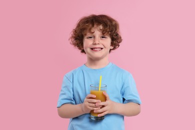 Cute little boy with glass of fresh juice on pink background