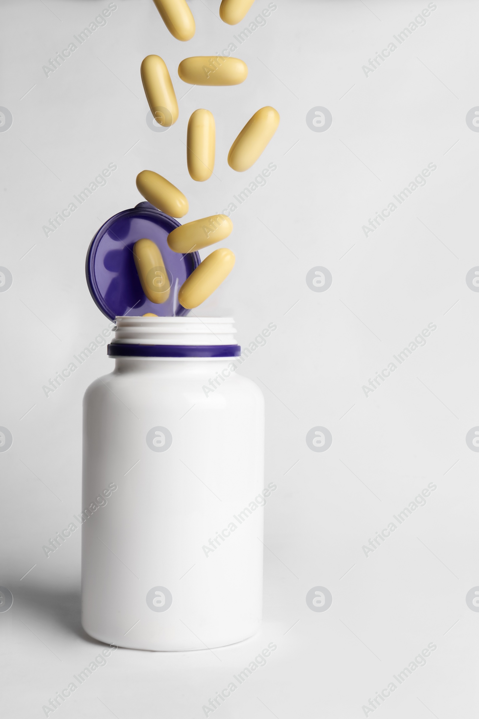 Photo of Pills falling into medical bottle on white background