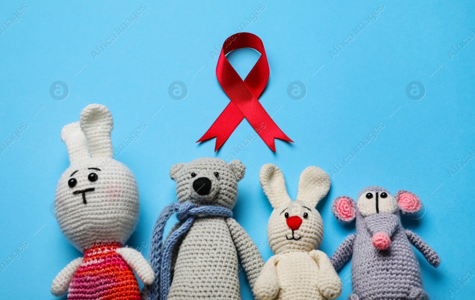 Photo of Cute knitted toys and red ribbon on blue background, flat lay. AIDS disease awareness