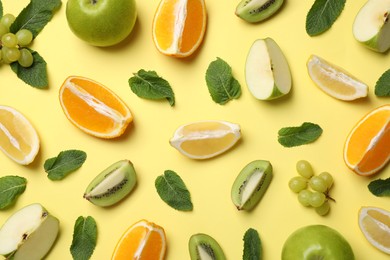 Different fresh ripe fruits and mint on yellow background, flat lay