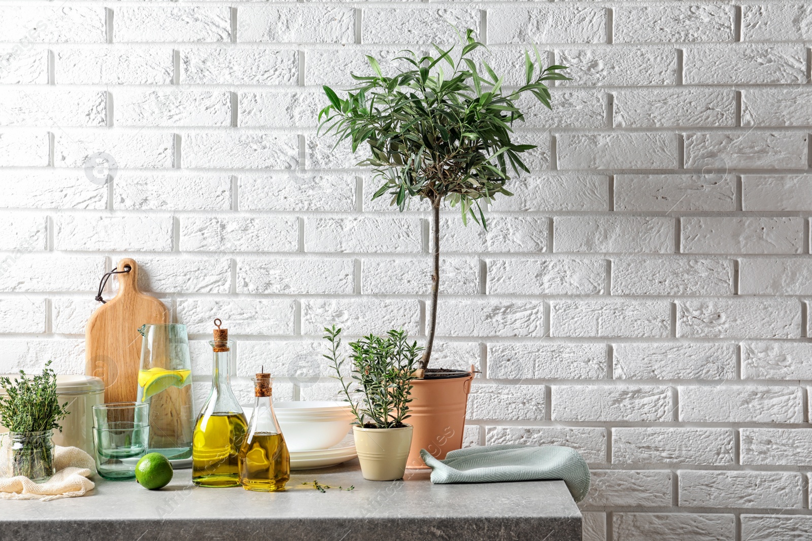 Photo of Fresh olive oil and kitchen utensils on table near brick wall