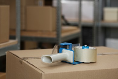 Photo of Adhesive tape dispenser on cardboard box indoors. Space for text