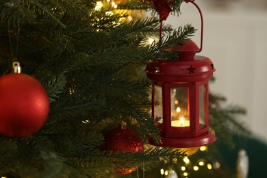 Photo of Christmas lantern with burning candle on fir tree against blurred background, closeup