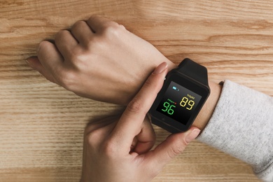 Image of Woman measuring oxygen level with smartwatch at wooden table, top view