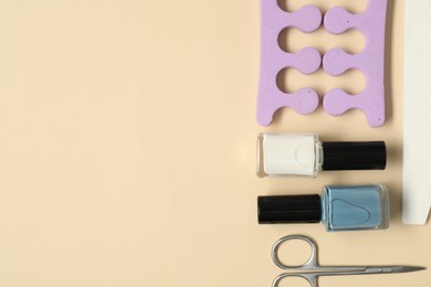 Photo of Nail polishes, scissors, toe separators and file on beige background, flat lay. Space for text