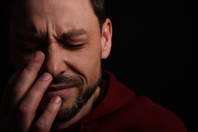 Photo of Sad man crying on black background, closeup. Space for text