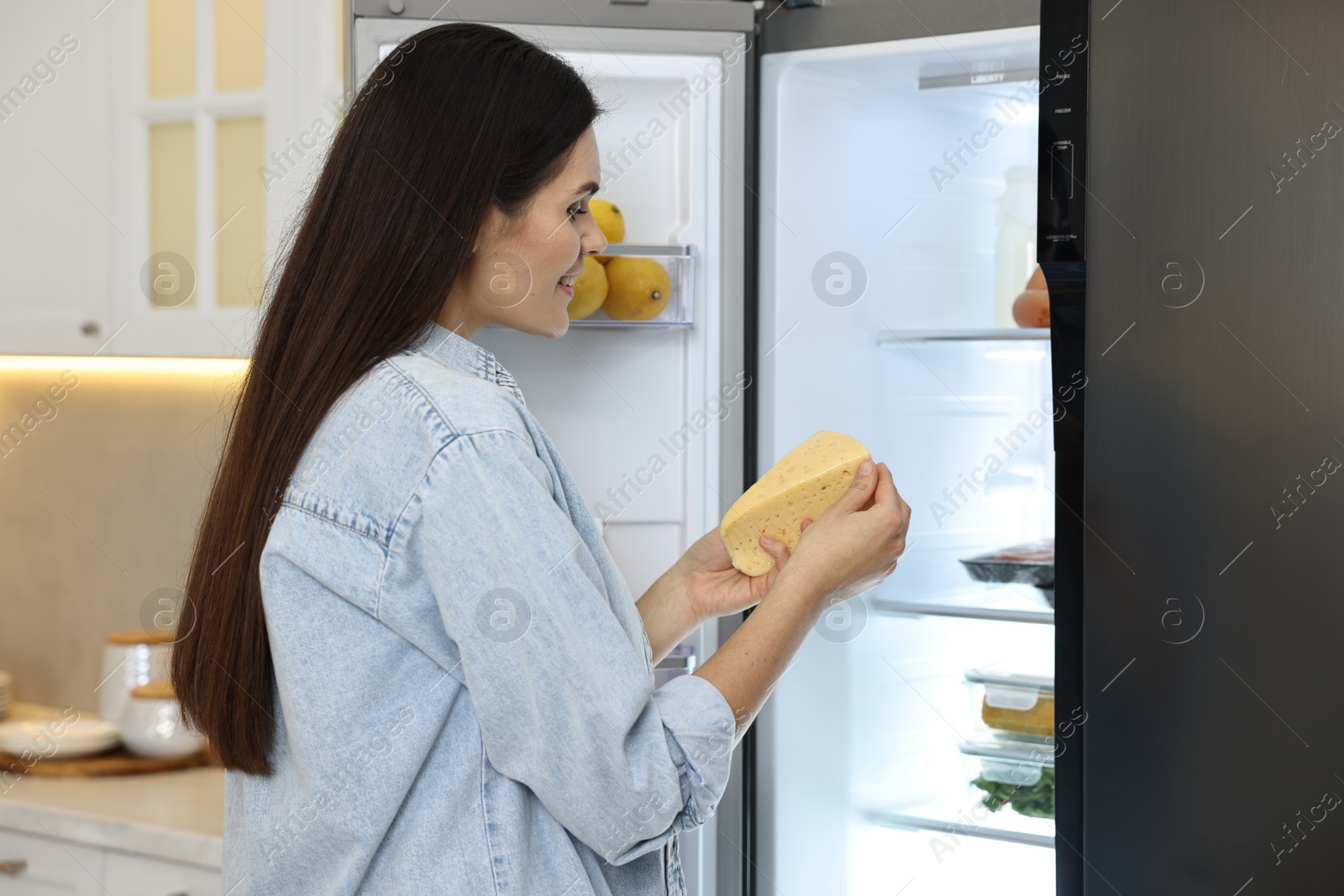 Photo of Young woman taking cheese out of refrigerator in kitchen