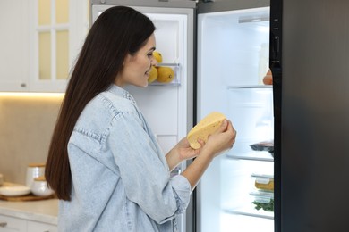 Photo of Young woman taking cheese out of refrigerator in kitchen