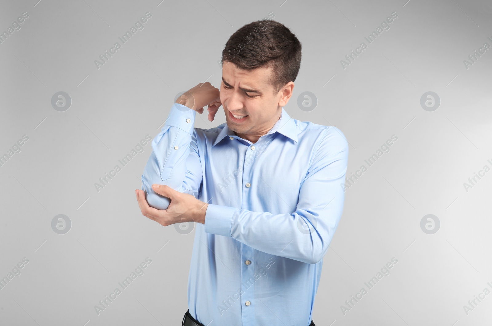 Photo of Young man suffering from pain in elbow on light background