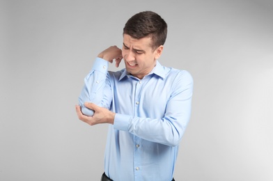 Photo of Young man suffering from pain in elbow on light background