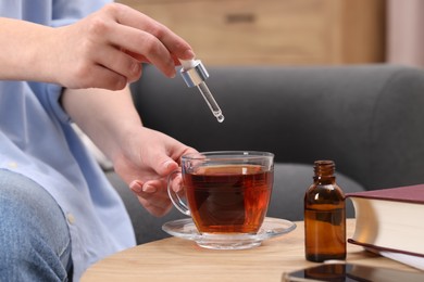 Woman dripping food supplement into cup of tea at wooden table indoors, closeup