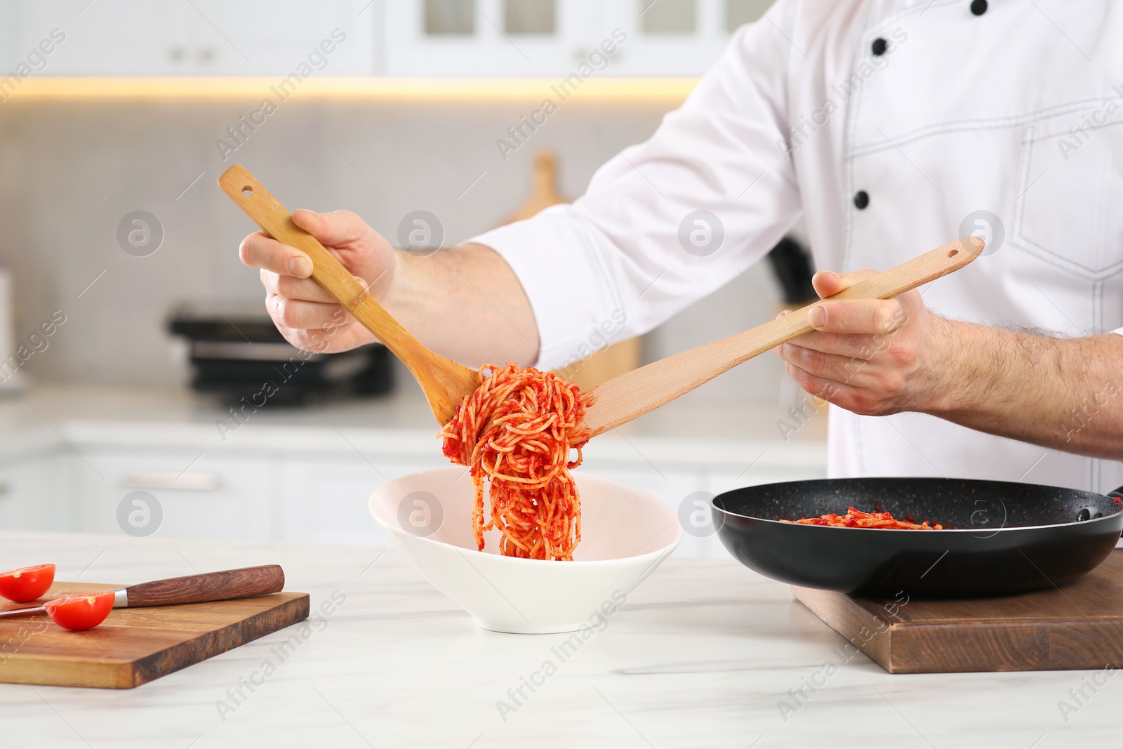 Photo of Professional chef putting delicious spaghetti into bowl at marble table in kitchen, closeup