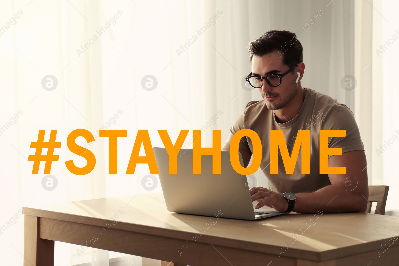 Image of Hashtag Stayhome - protective measure during coronavirus pandemic. Young man working on laptop at table near window