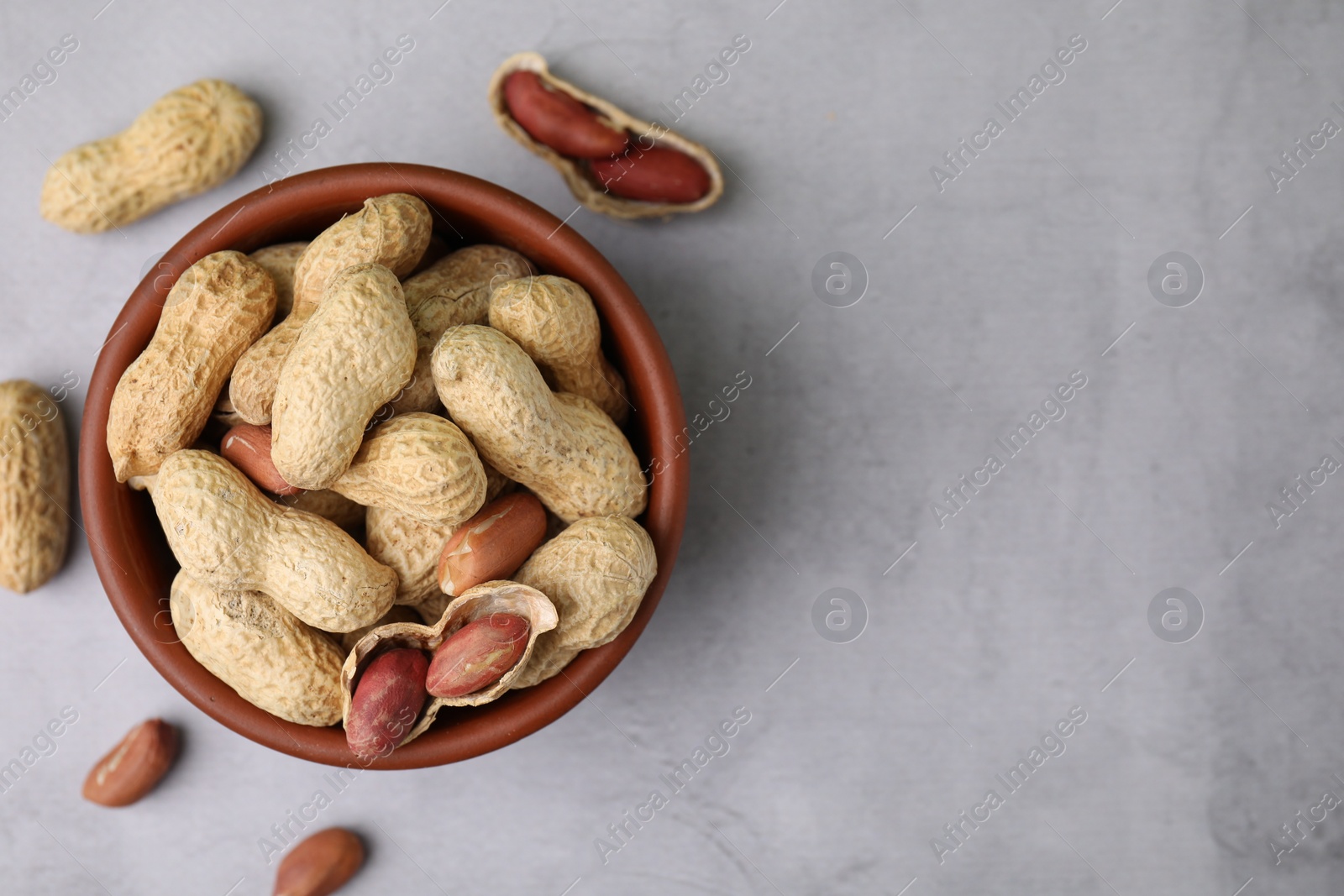 Photo of Fresh unpeeled peanuts in bowl on grey table, top view. Space for text