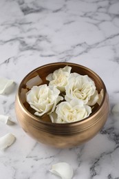 Photo of Tibetan singing bowl with water and beautiful roses on white marble table