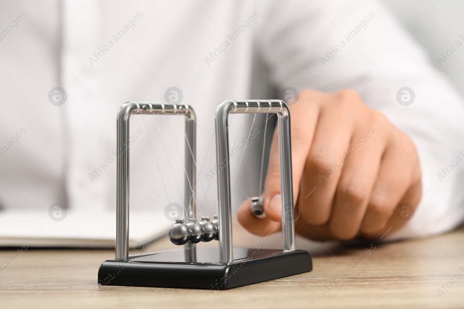 Photo of Man playing with Newton's cradle at table, closeup. Physics law of energy conservation