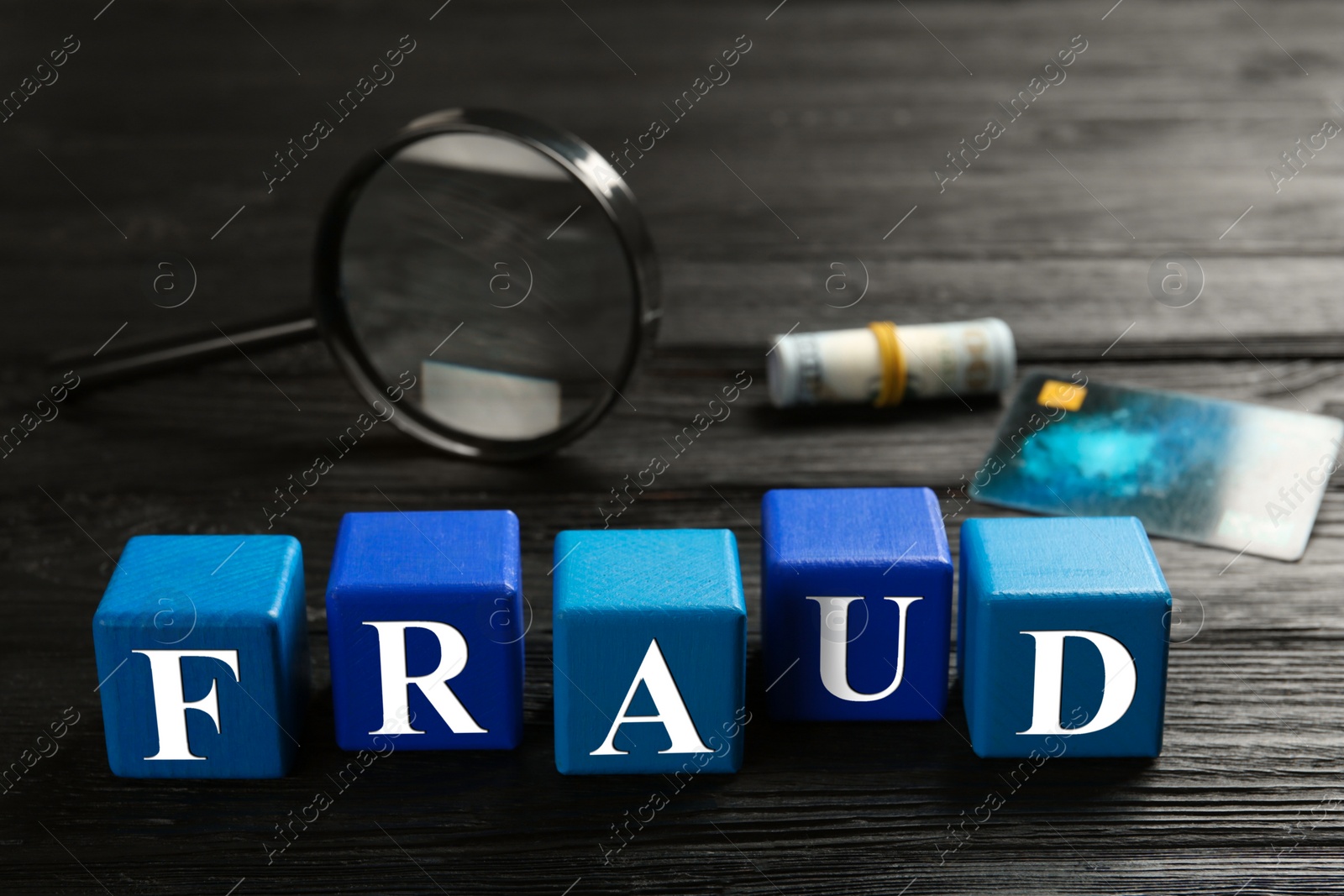 Photo of Cubes with word Fraud, credit card, rolled dollar banknotes and magnifying glass on black wooden table