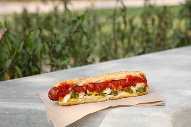 Photo of Fresh tasty hot dog with ketchup on light grey parapet outdoors